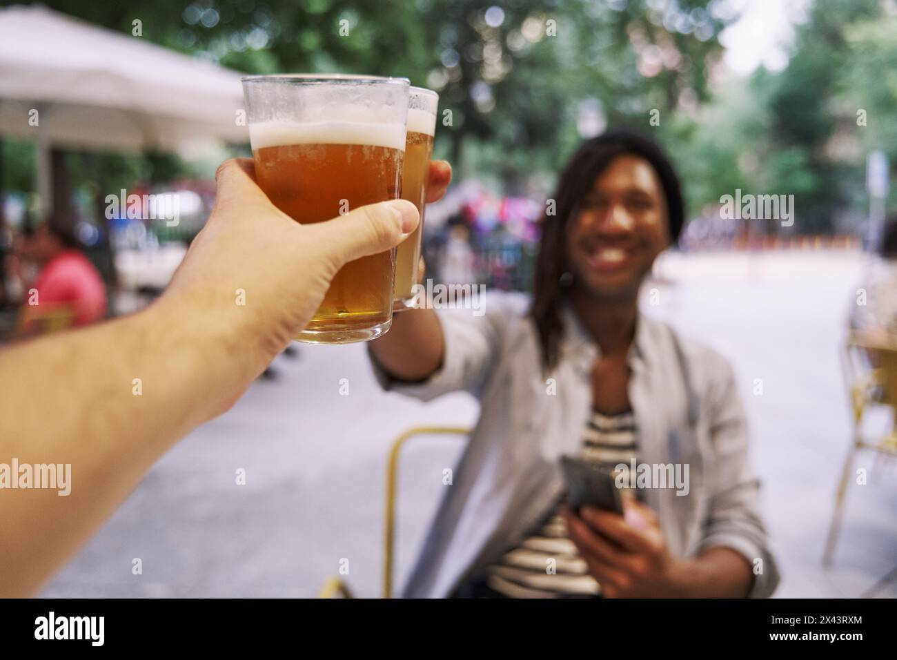 An unrecognizable couple toasting with beer on a bar terrace on a date. Stock Photo