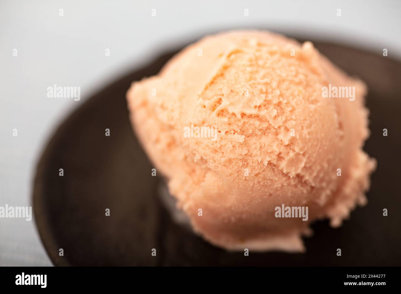 A fresh scoop of homemade strawberry ice cream in a black bowl Stock Photo