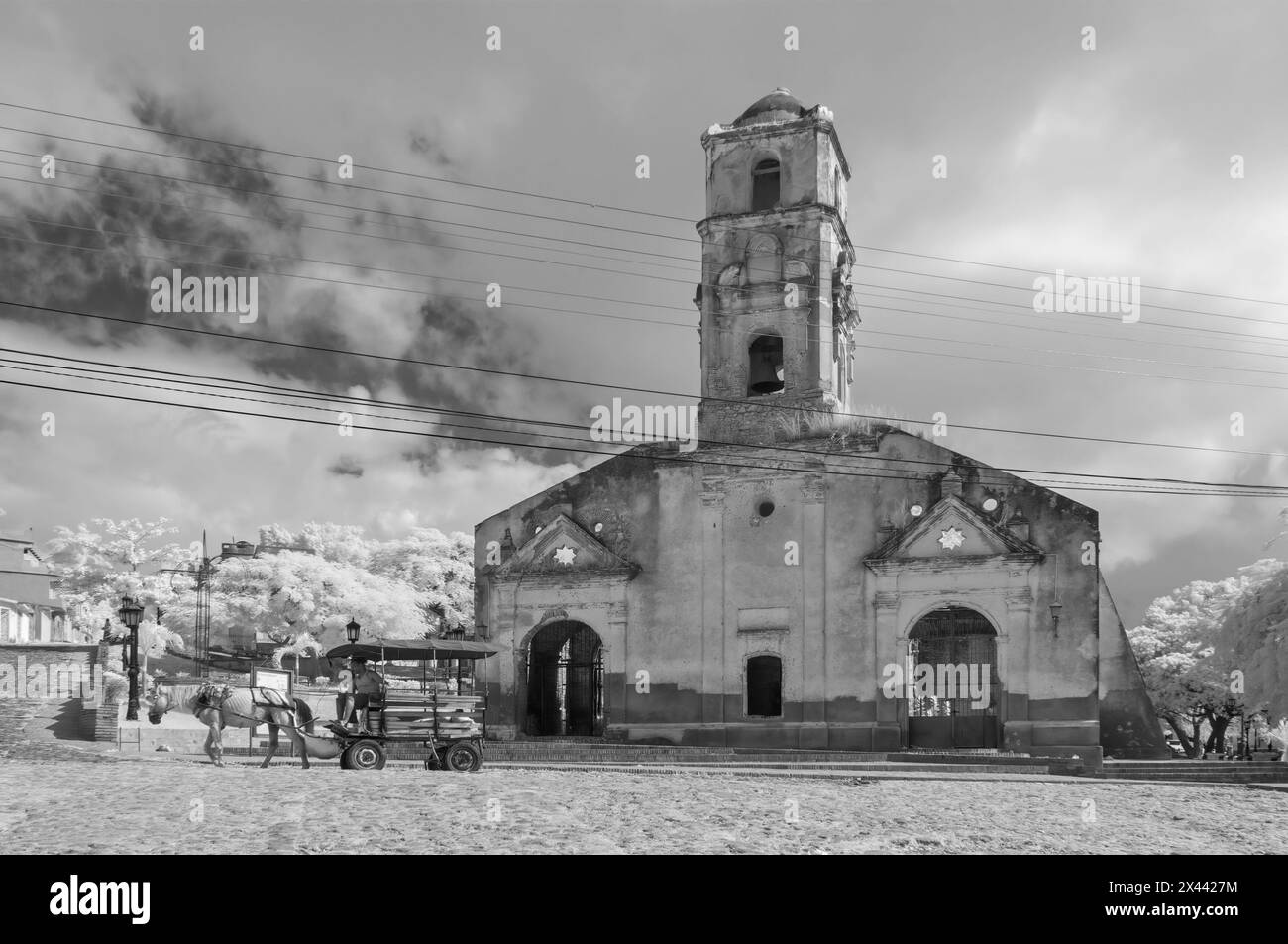 An infrared picture of a horse and cart crossing the cobbles in front of Santa Ana Church, Plaza Sant Ana, Trinidad, Cuba. Stock Photo
