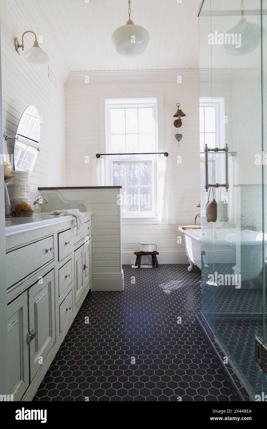 White antique style finish vanity with quartz countertop and two sunken sinks, freestanding claw foot bathtub, glass shower stall in kid's upstairs Stock Photo