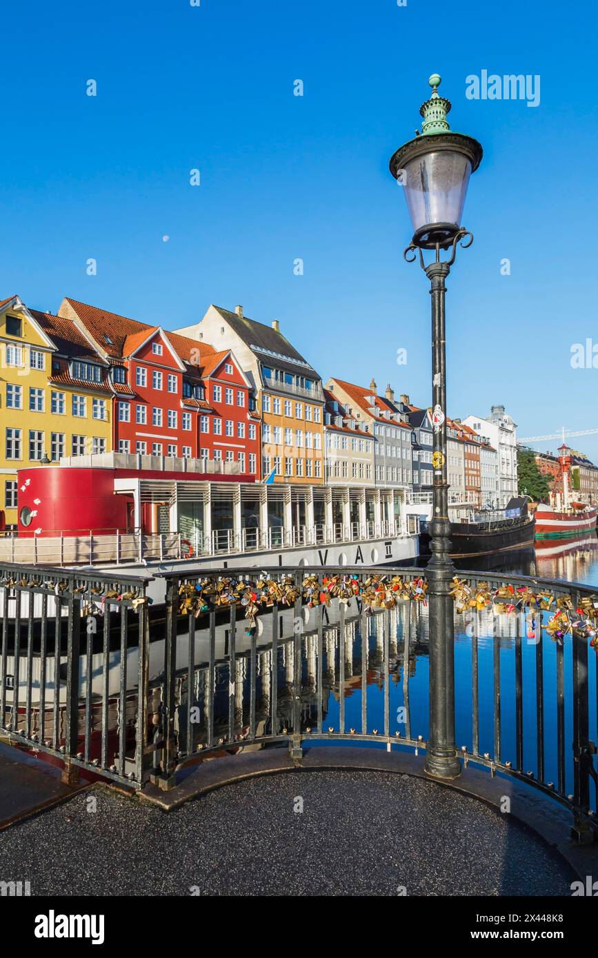 Love locks on black metal railing of canal bridge with antique lamppost, moored boats and colourful 17th century apartment buildings and houses Stock Photo