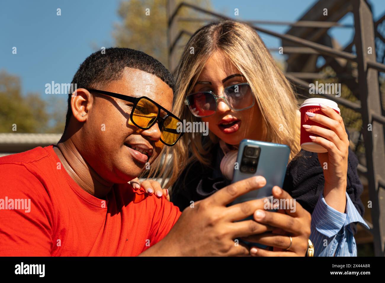 Happy interracial couple checking cell phone outdoors. Stock Photo