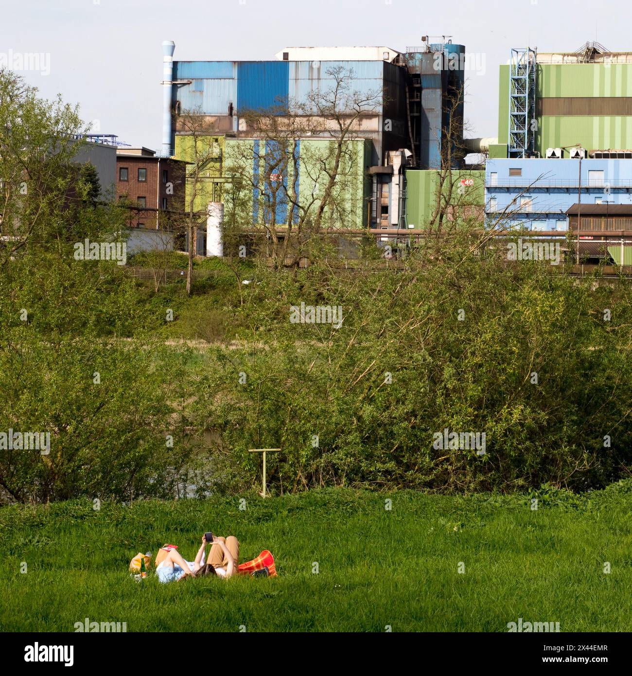 Couple lies on the Ruhrauen in front of the stainless steel plant in Witten, Ruhr area, North Rhine-Westphalia, Germany Stock Photo