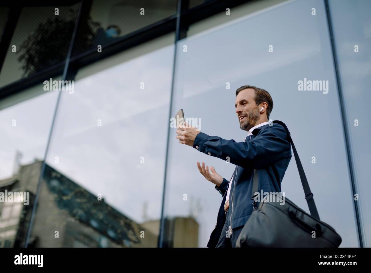 Low angle view of businessman on video call using smart phone while standing against glass building Stock Photo