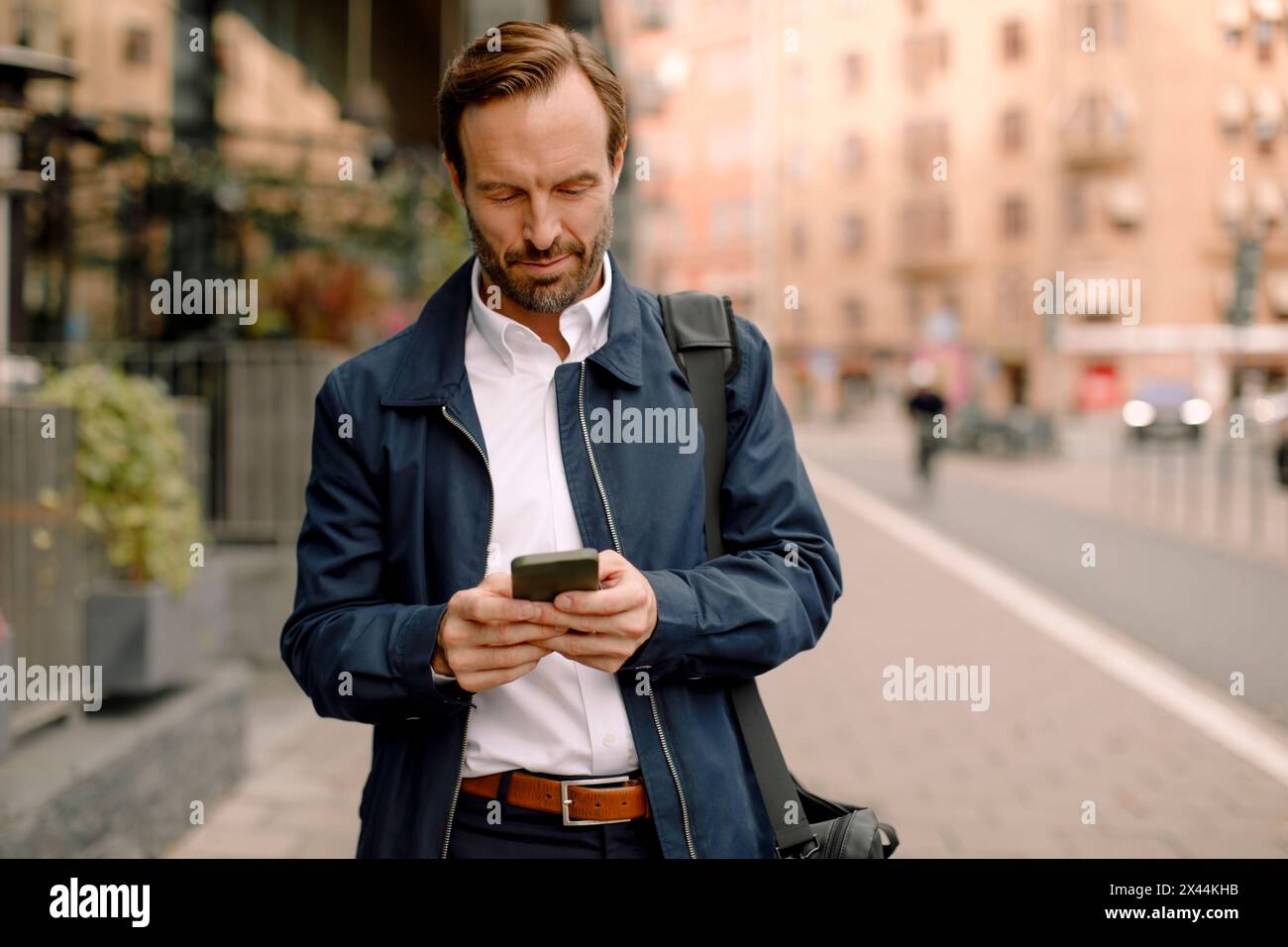 Businessman using smart phone while walking on sidewalk in city Stock Photo