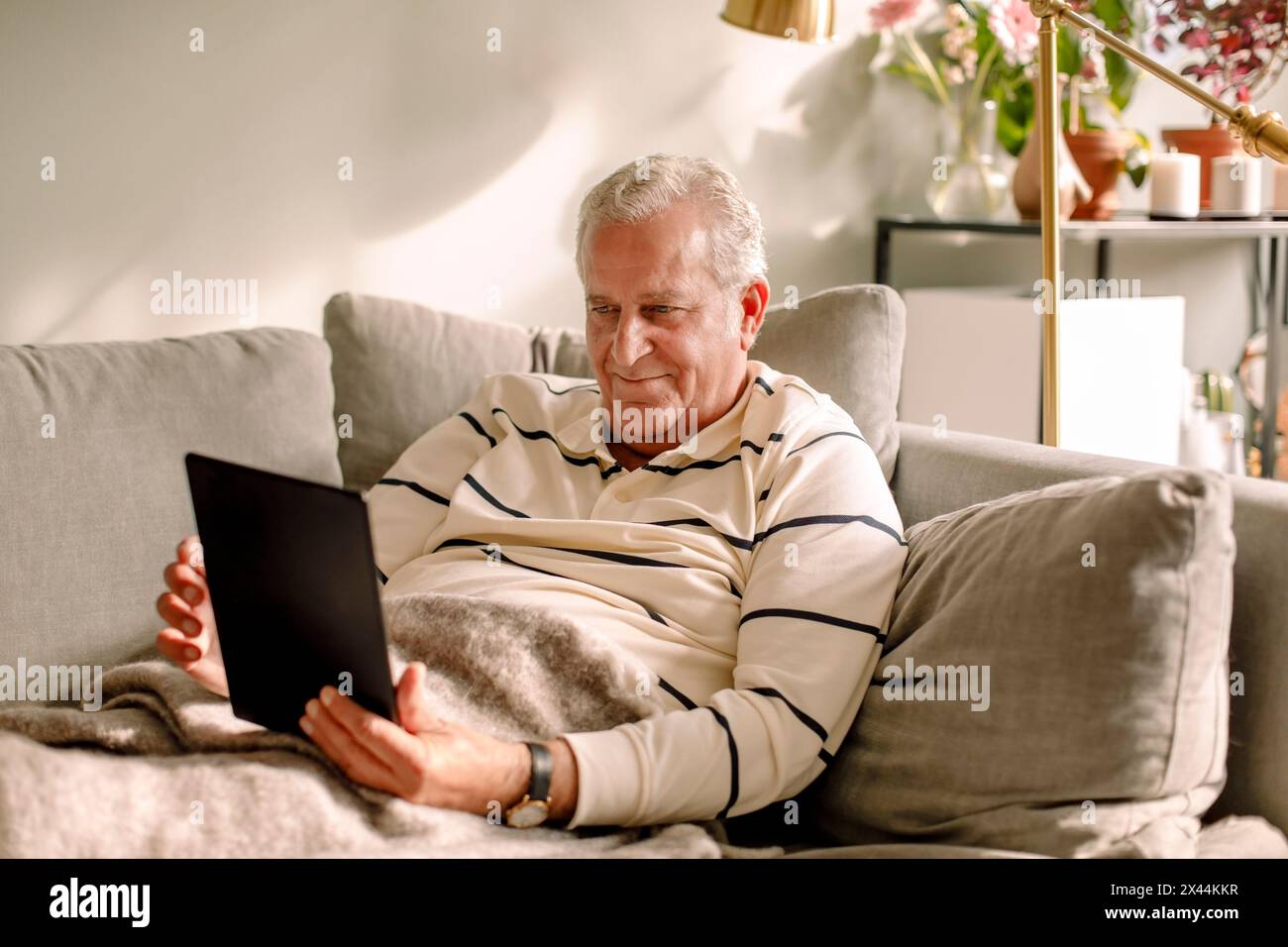Retired senior man using digital tablet while sitting on sofa Stock Photo