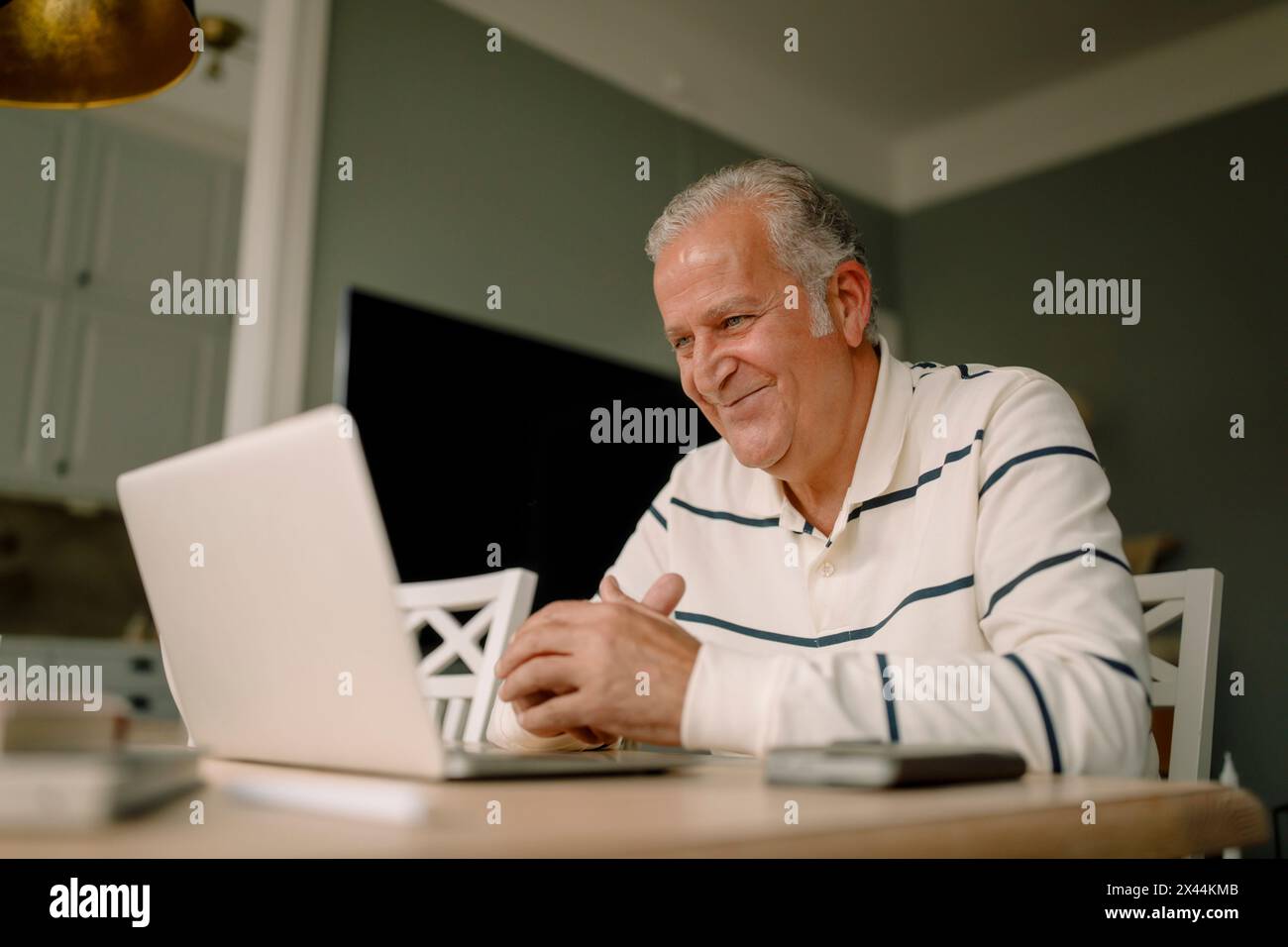 Smiling retired senior man using laptop at dining table in kitchen Stock Photo