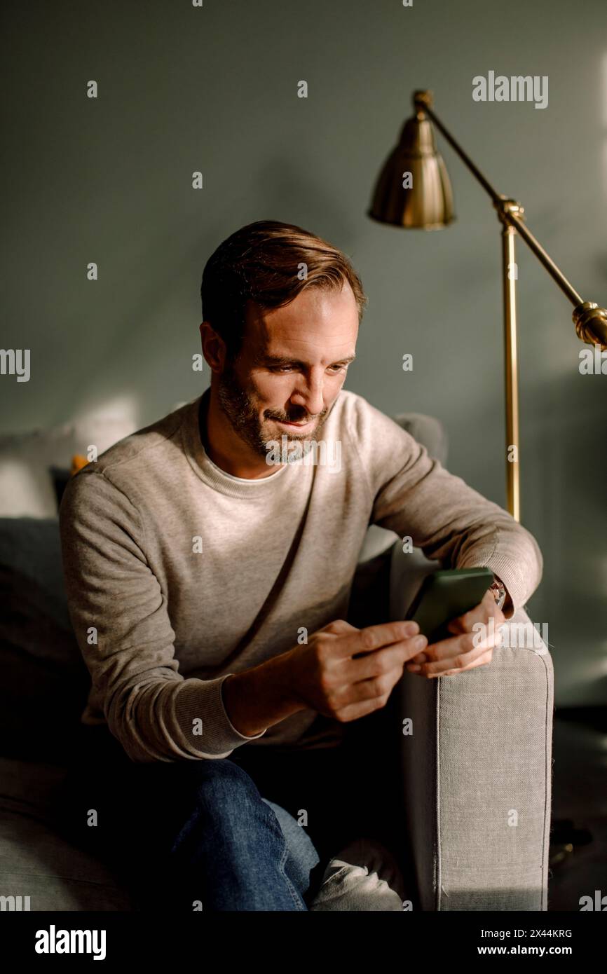 Mature man using smart phone while sitting on sofa at home Stock Photo