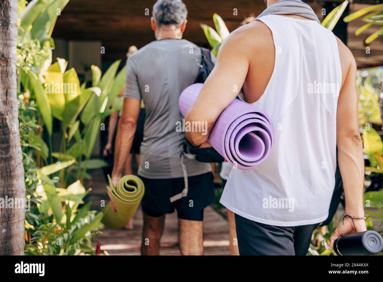 Rear view of men holding rolled up yoga mats while walking towards resort Stock Photo