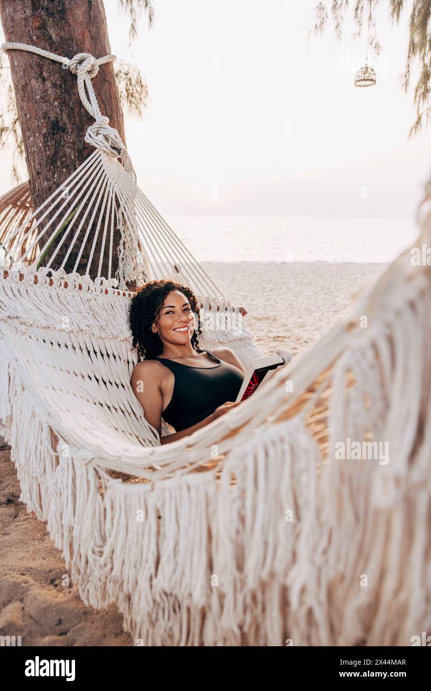 Portrait of smiling mature woman lying down in hammock at beach Stock Photo