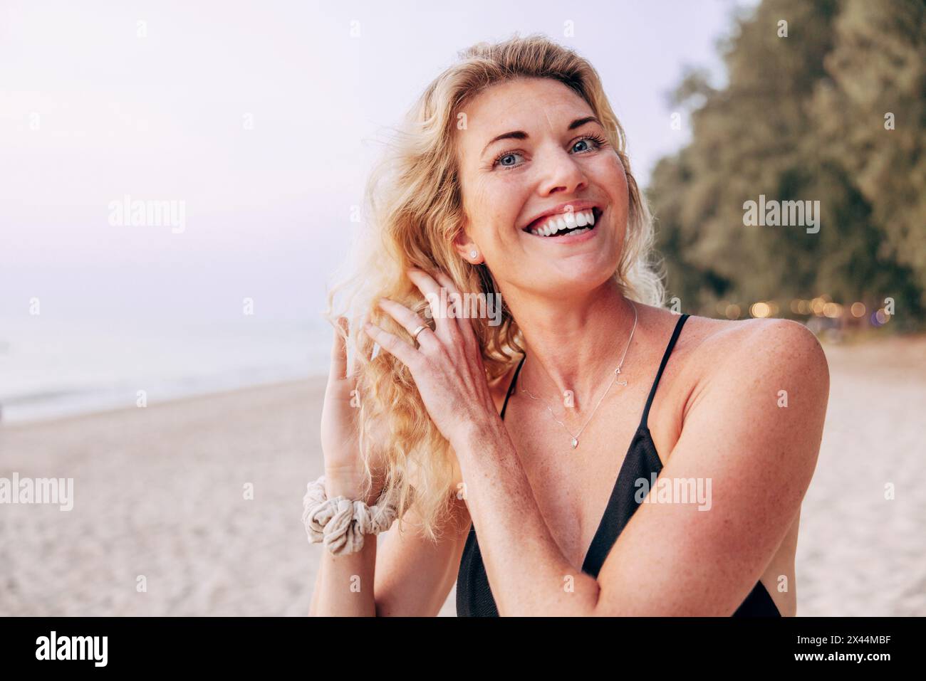 Happy blond woman with hands in hair on vacation at beach Stock Photo