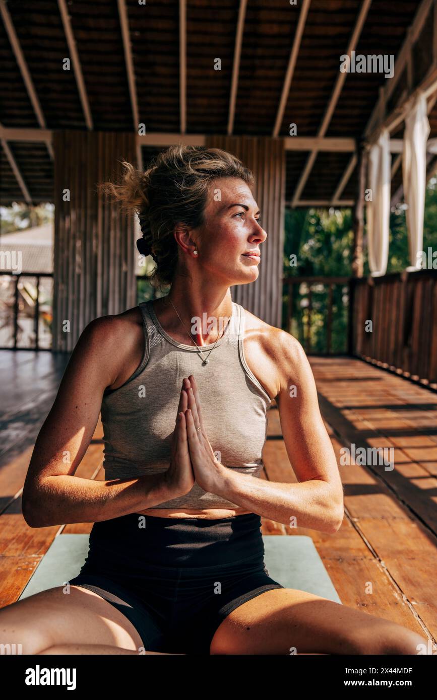 Woman doing yoga while sitting with hands clasped on floor at wellness resort Stock Photo