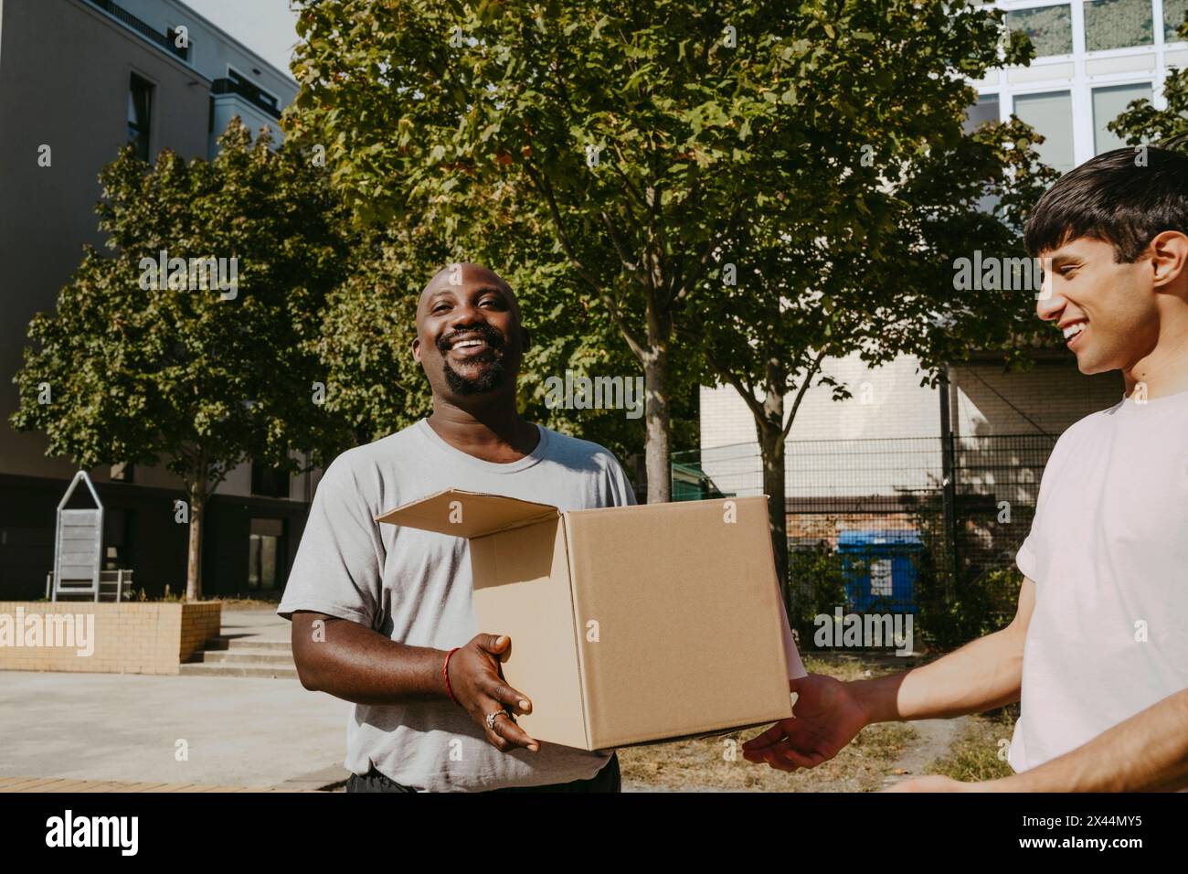 Smiling male volunteer passing donation box to teammate during charity drive at community center Stock Photo