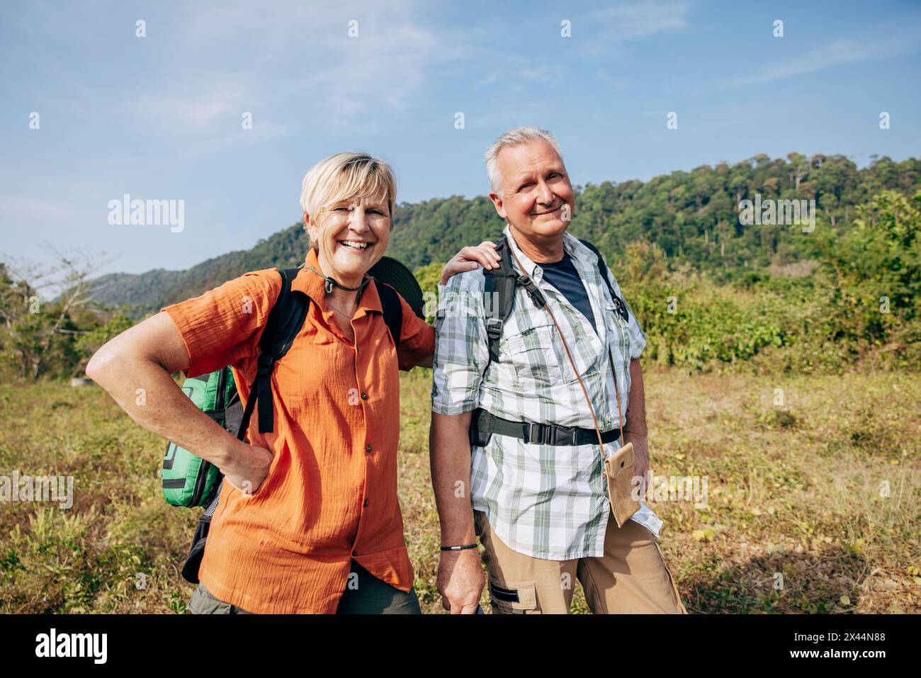 Portrait of smiling senior male and female tourists standing on grass at sunny day Stock Photo
