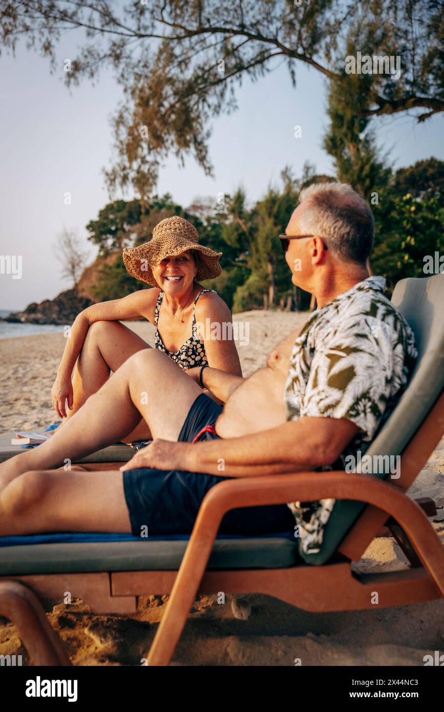 Happy senior couple having fun while sitting on deck chair at beach Stock Photo