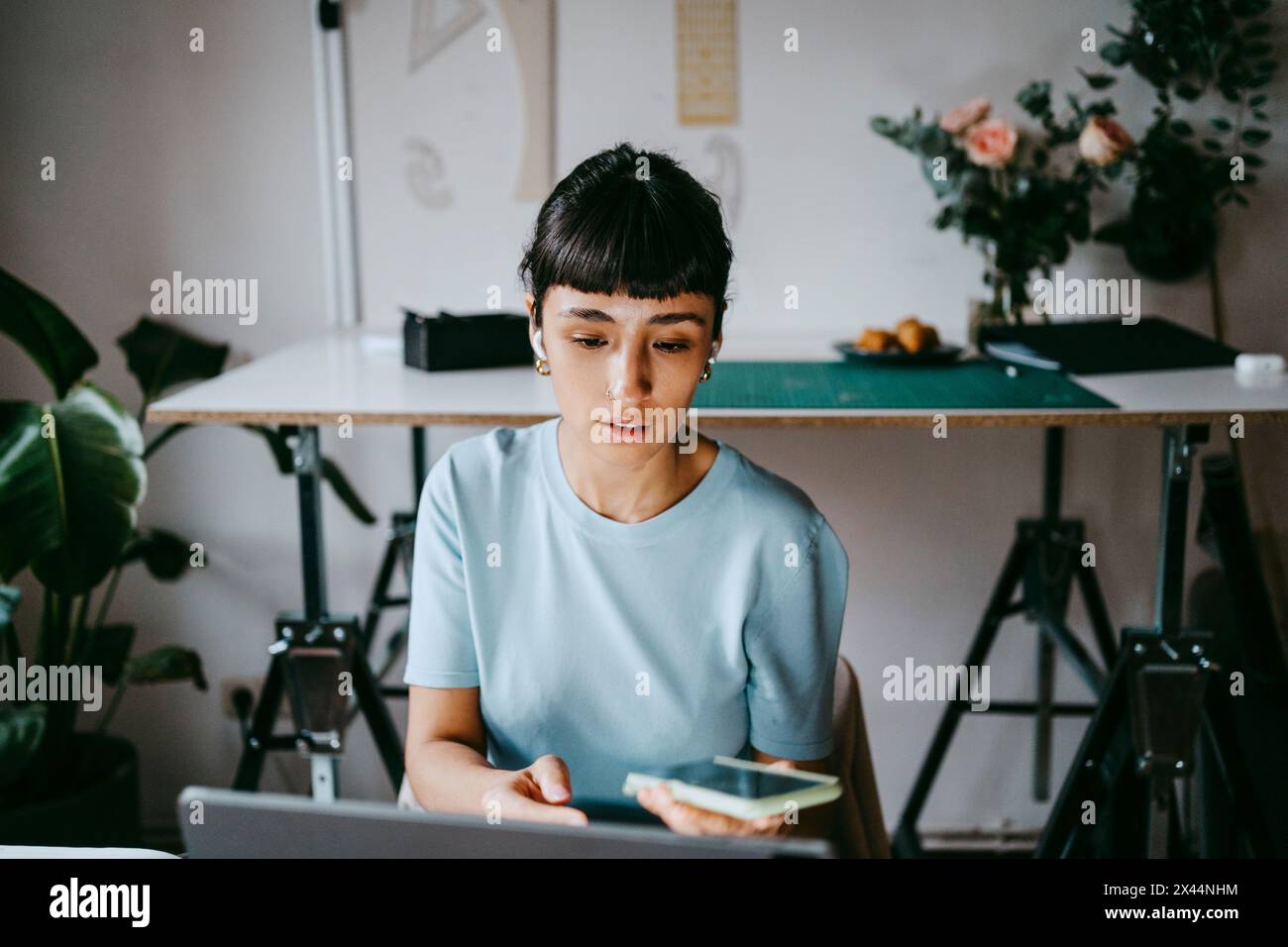 Young female freelancer talking through smart phone while using laptop at home Stock Photo