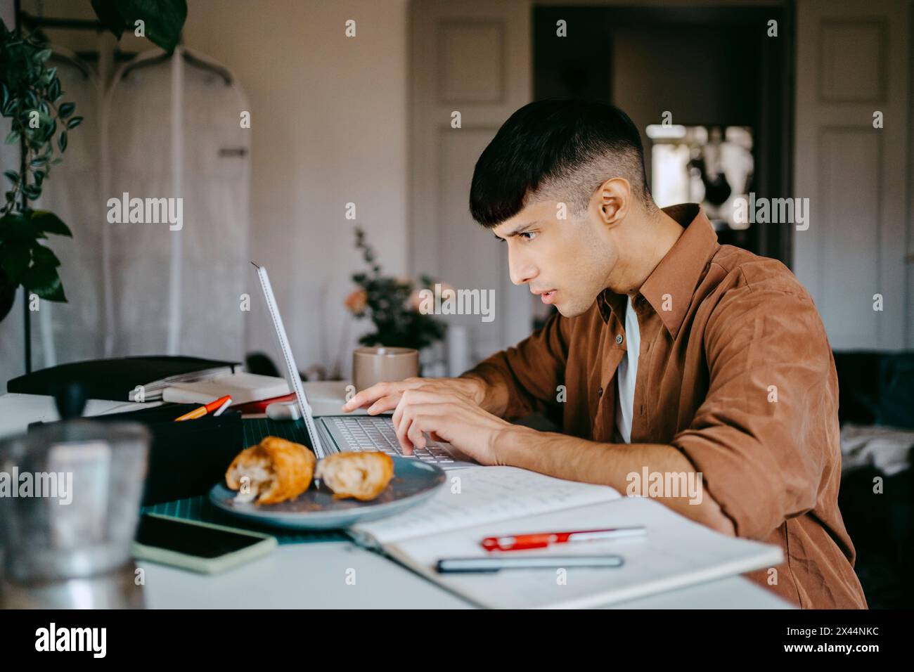 Focused male freelancer using laptop at desk while working from home Stock Photo