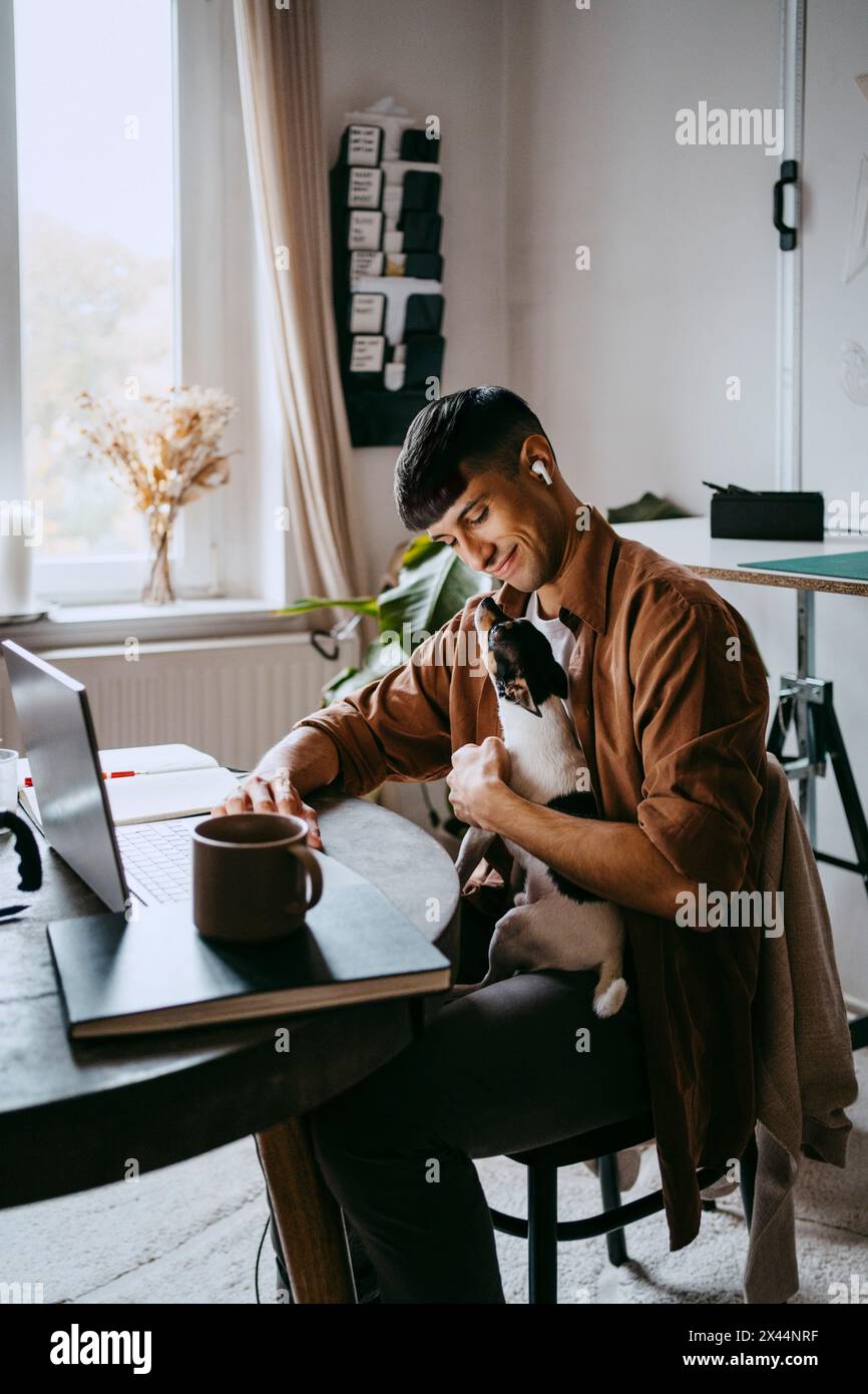 Smiling male freelancer sitting with pet dog at home office Stock Photo