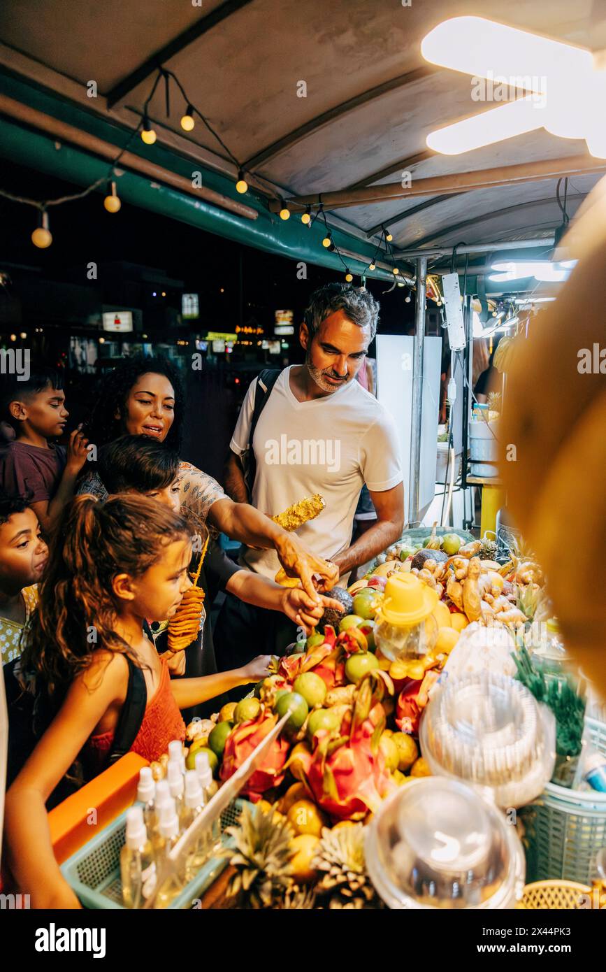 Tourist family choosing fruits from stall at food market Stock Photo
