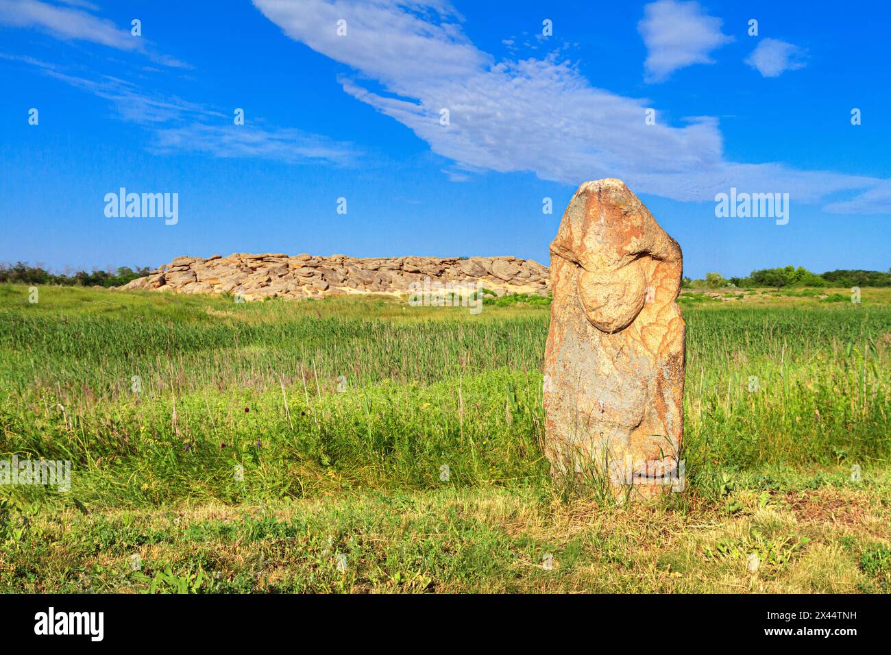 View of the ancient kurgan stela, stone idol against the backdrop of ancient mound of sandstone boulders, in the archeological preserve Kamyana Mohyla Stock Photo