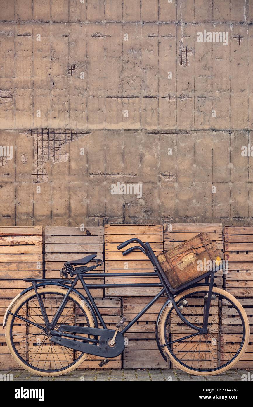 Vintage black cargo transport bicycle with crate carrier in front of old wooden crates and concrete wall Stock Photo