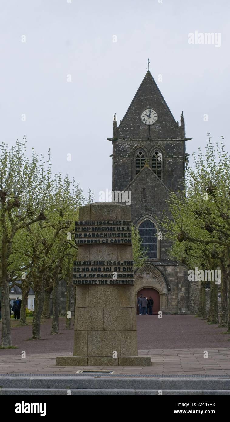 Sainte-Mere-Eglise, France - Apr 19, 2024: Sainte-Mere-Eglise church. People walking in Sainte-Mere-Eglise. Streets and buildings. Lifestyle in the ur Stock Photo