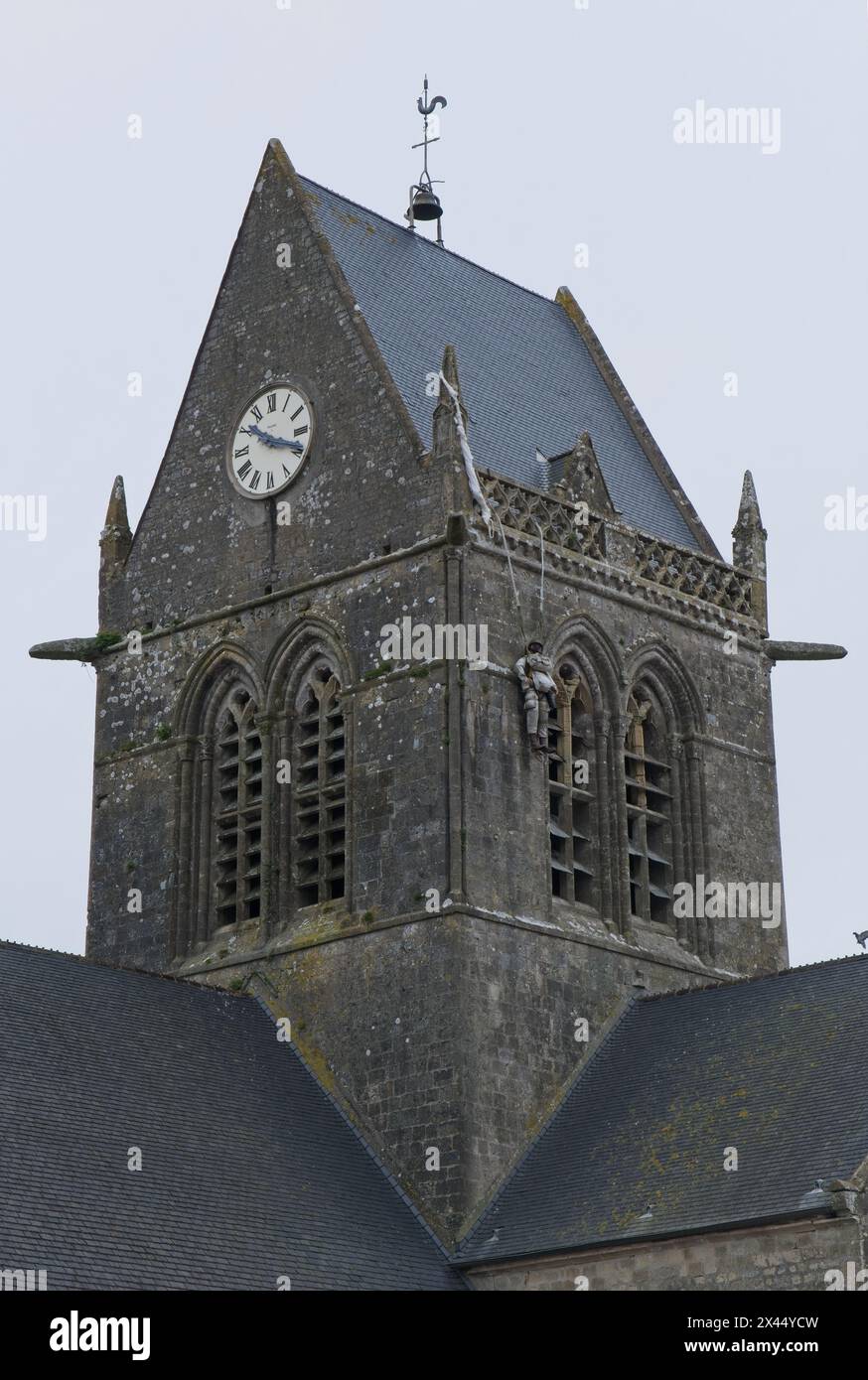 Sainte-Mere-Eglise, France - Apr 19, 2024: Sainte-Mere-Eglise church. People walking in Sainte-Mere-Eglise. Streets and buildings. Lifestyle in the ur Stock Photo