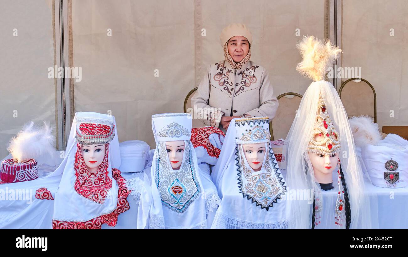 Almaty, Kazakhstan - March 18, 2024: A senior Asian woman selling in a sales tent at a crafts fair. Women's traditional national Kazakh headdresses wi Stock Photo