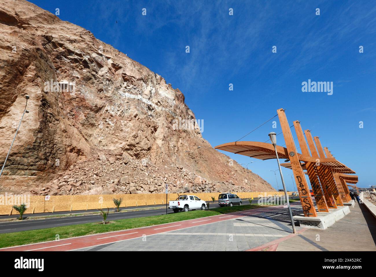 Wide angle view of wooden bus shelter and vehicles parked on Av Costanera / Av. Comandante San Martín below cliffs of El Morro headland, Arica, Chile Stock Photo