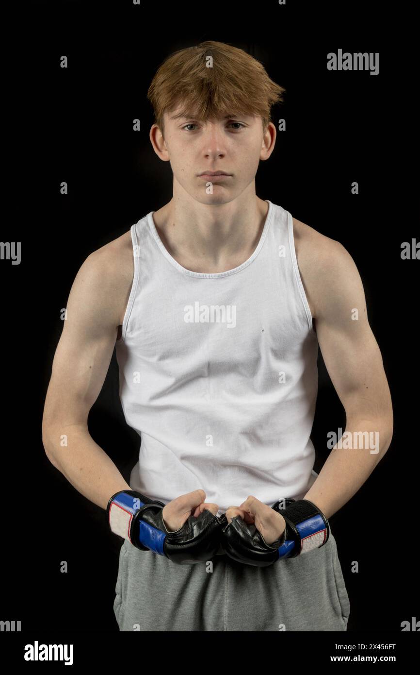 A 15 year old male teenager boxer, against a black background,  wearing a sleevless top, flexing Stock Photo
