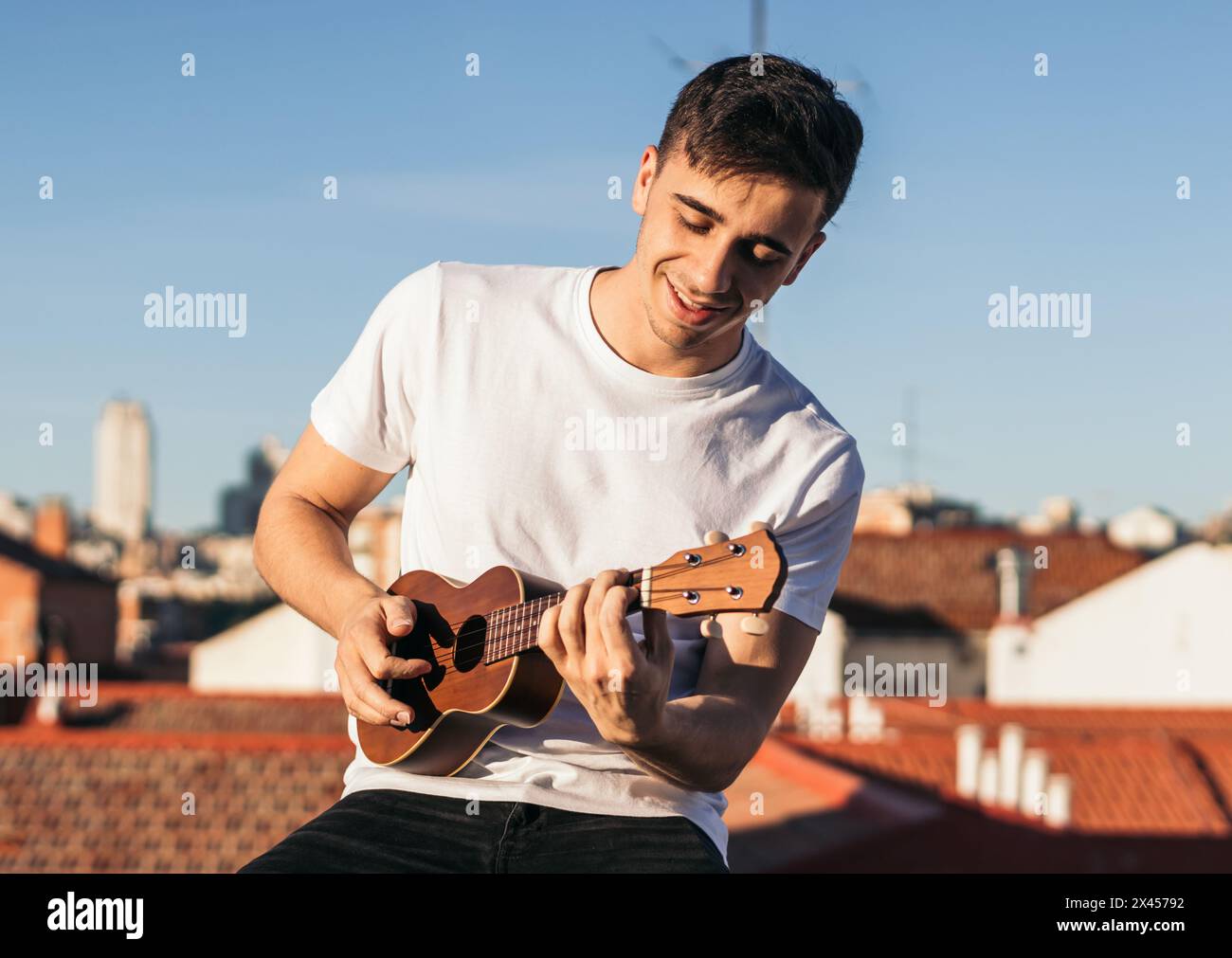 smiling man playing ukelele on a rooftop Stock Photo