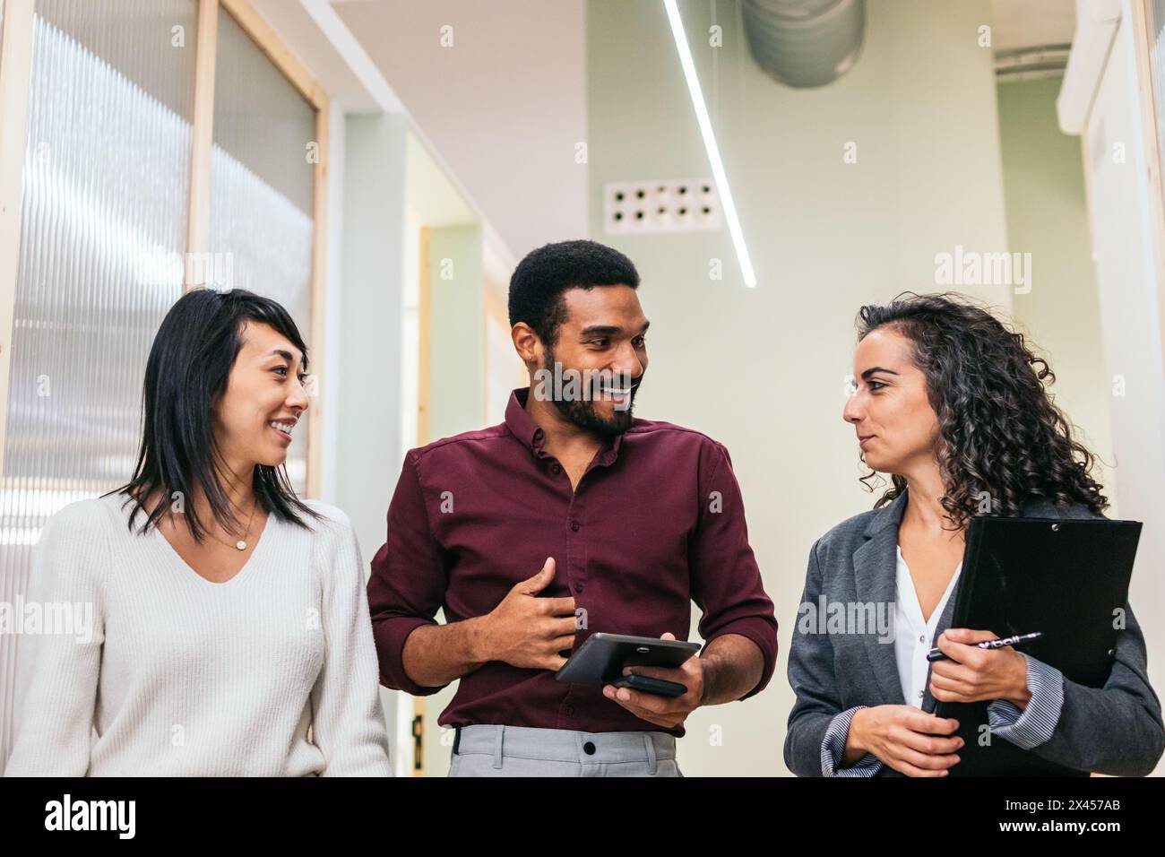Multiracial coworkers talking happily in office corridor Stock Photo