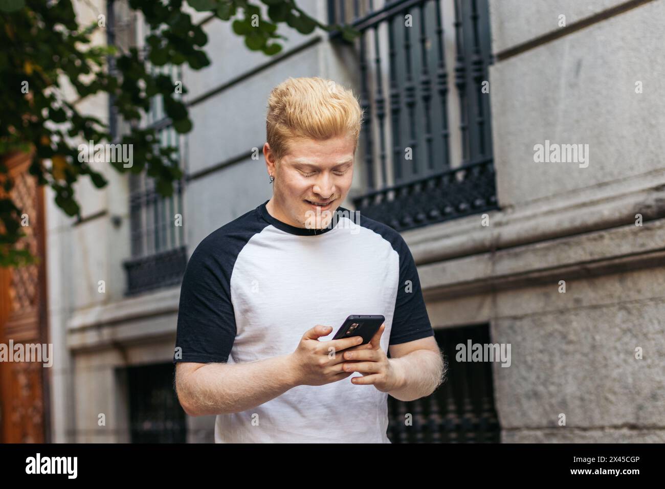 Young Albino latin man walking down the street using smartphone Stock Photo