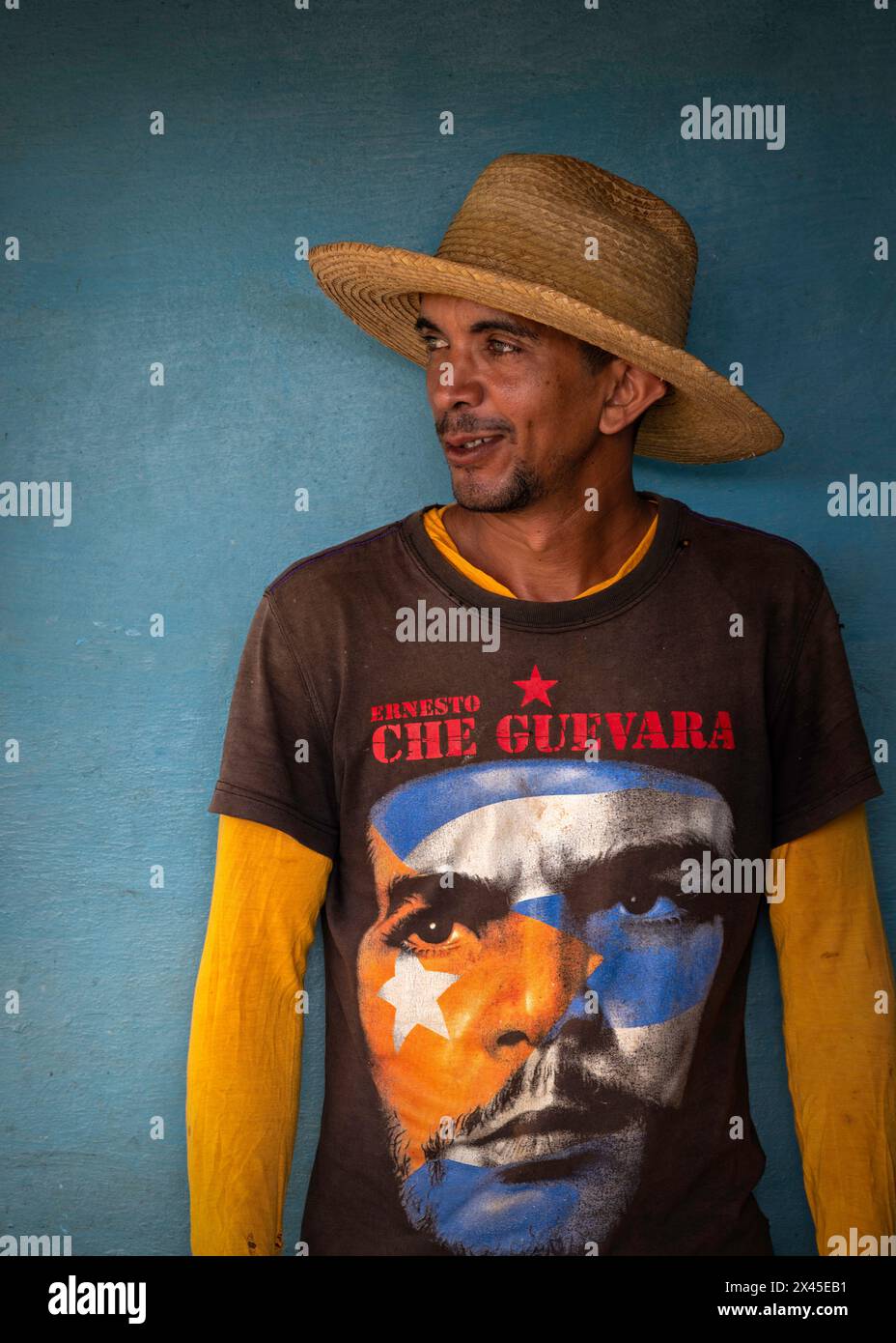 A young man wearing a sombrero and a Che Guevara tee shirt stood against the blue wall of a farmhouse in the Vinales Valley, Vinales, Cuba. Stock Photo