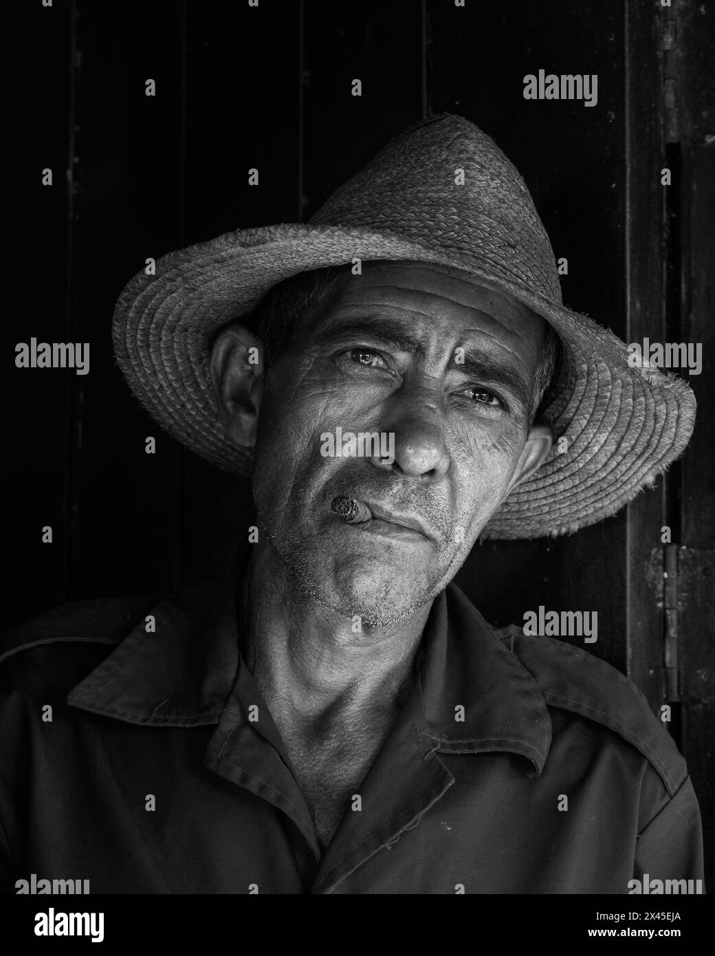 A tobacco farmer wearing a straw hat smoking a cigar by the front door of his farmhouse in the Vinales Valley, Vinales, Cuba. Stock Photo