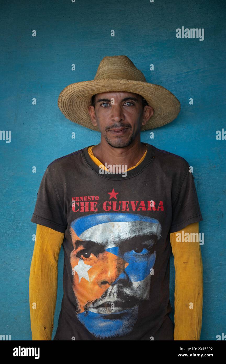 A young man wearing a sombrero and a Che Guevara tee shirt stood against the blue wall of a farmhouse in the Vinales Valley, Vinales, Cuba. Stock Photo