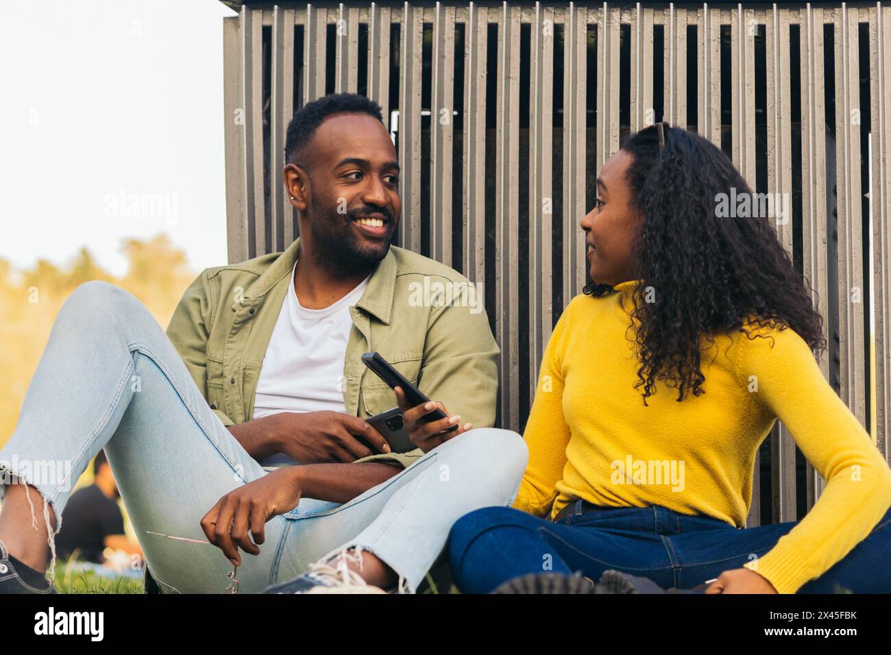 black couple sitting in a park using mobile Stock Photo