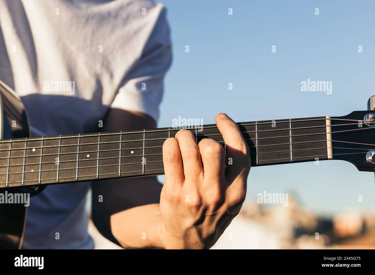 young man sitting playing acoustic guitar close-up Stock Photo