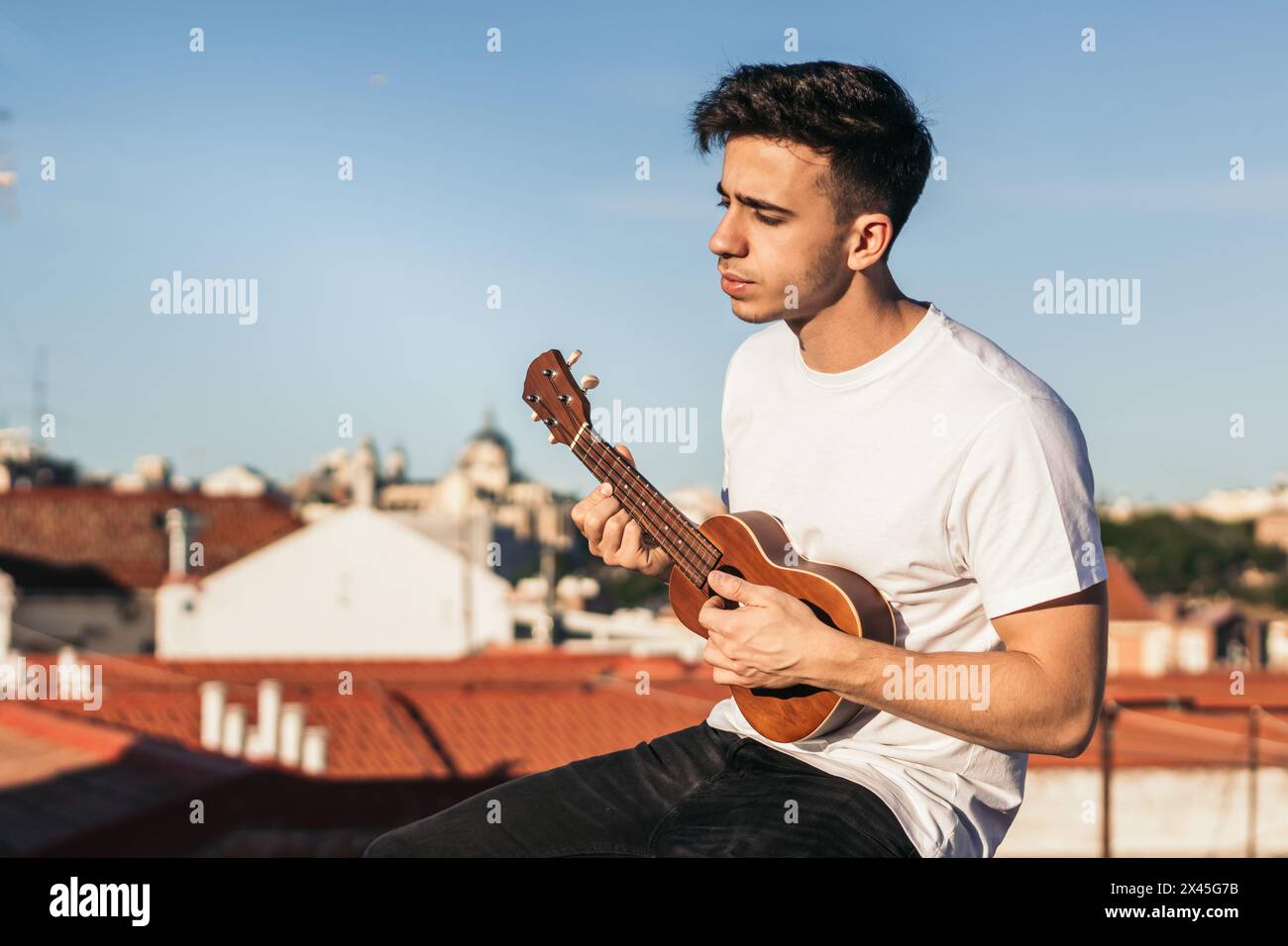 young man sitting playing ukelele on a rooftop Stock Photo