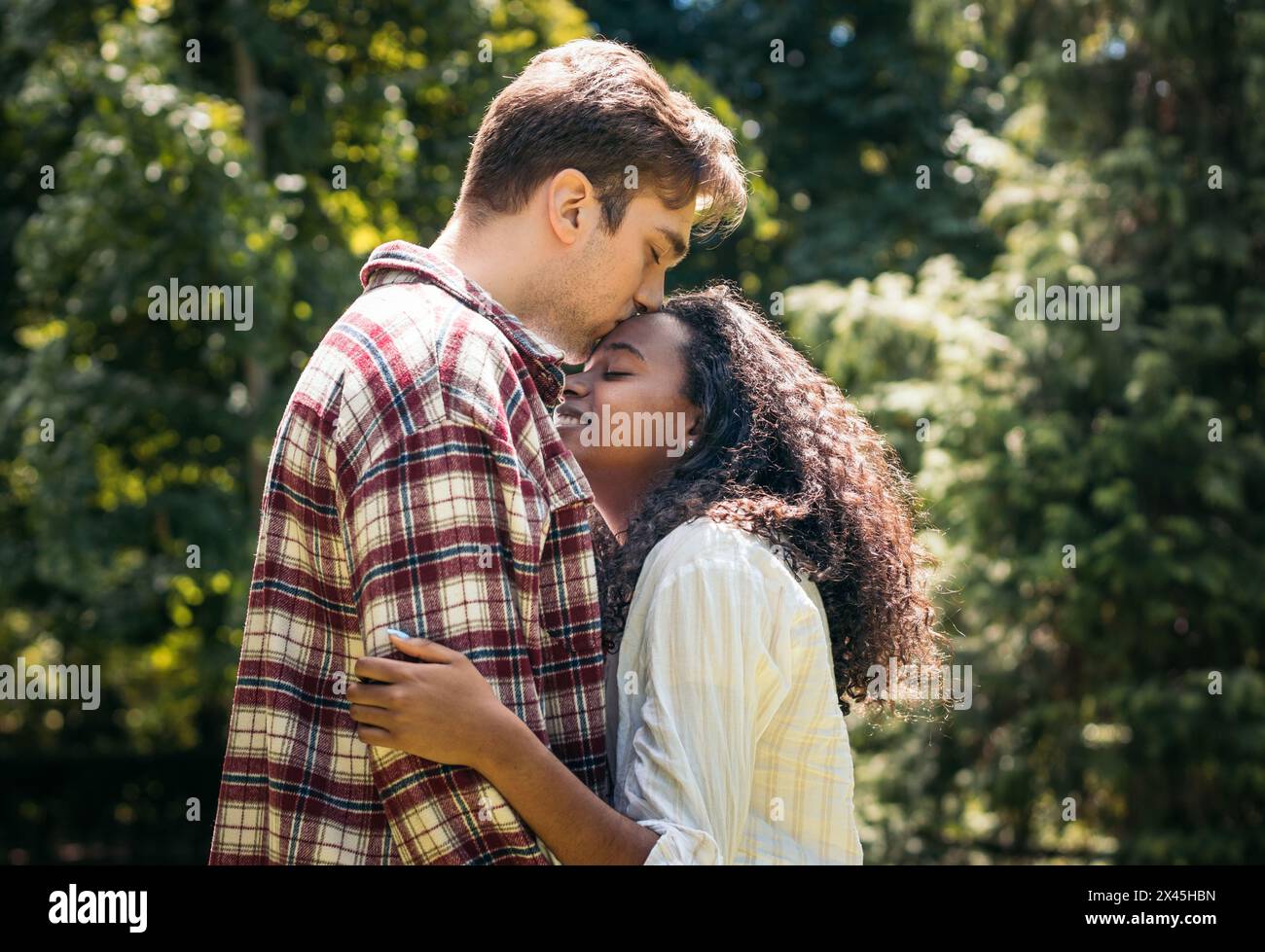 Interracial young couple hugging and kissing in the park Stock Photo ...