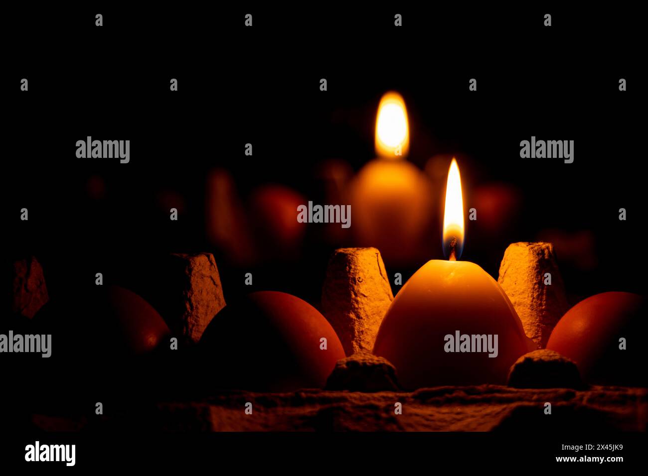 A yellow candle in the shape of an egg in the dark on a tray with chicken eggs stands near a mirror, Easter holiday Stock Photo