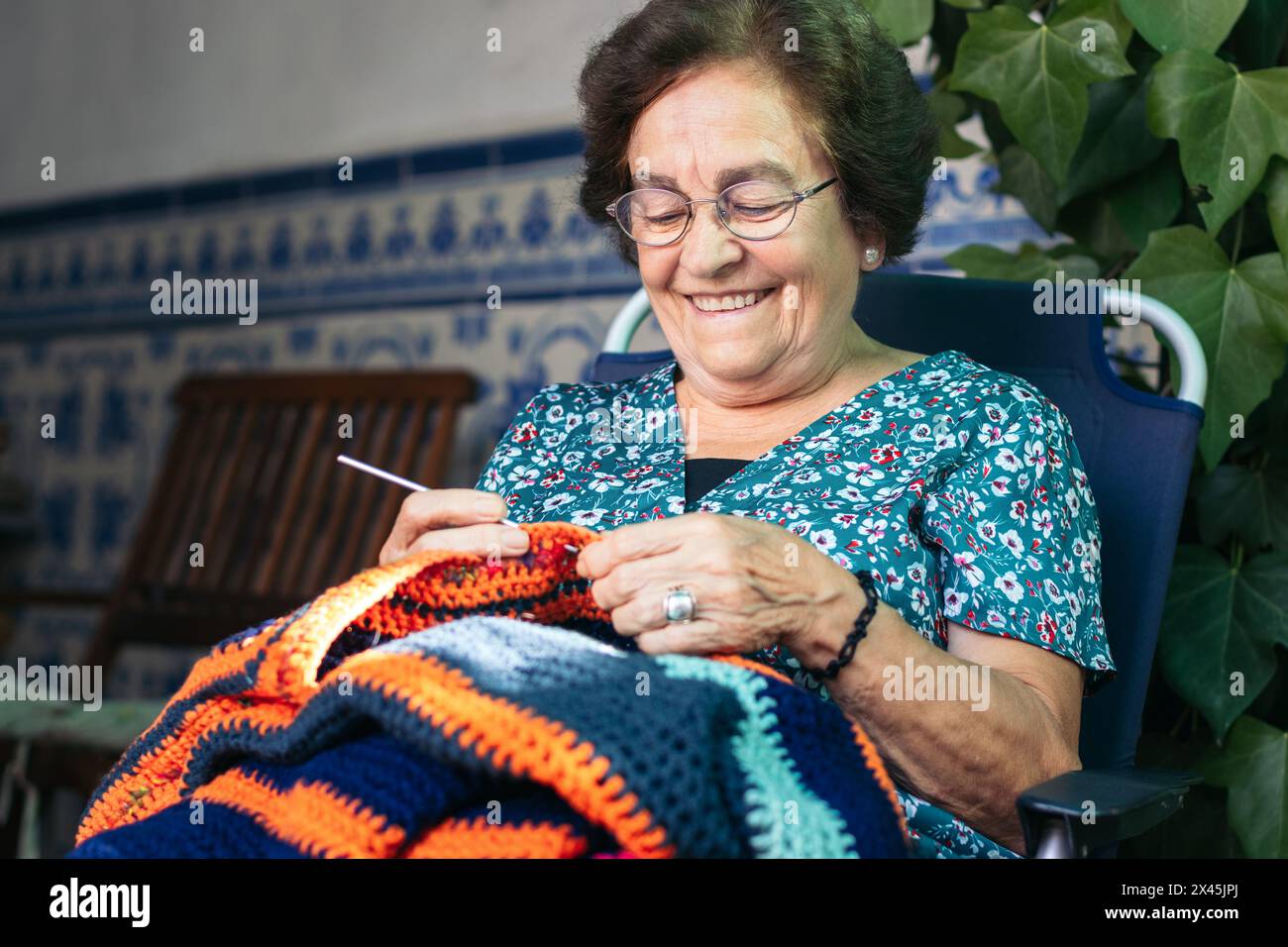 Elderly woman crocheting a blanket. She is sitting in a chair in the ...