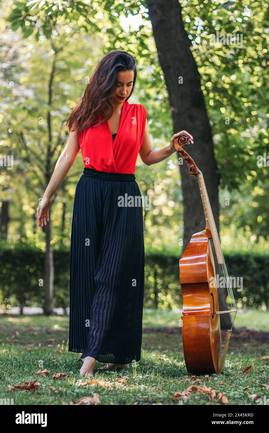 female musician standing holding her cello in a park Stock Photo - Alamy