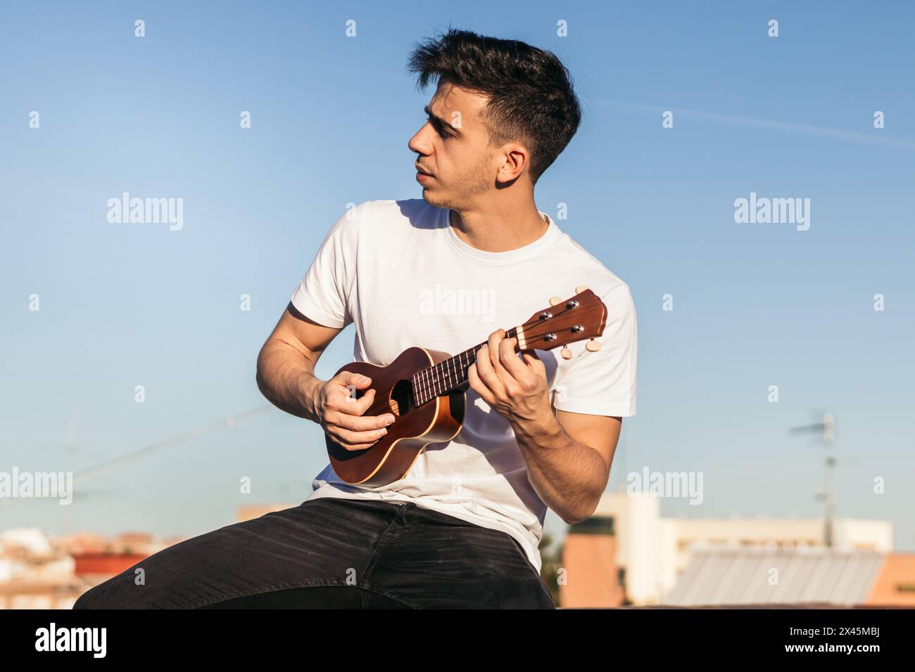 young man sitting playing ukelele on a rooftop Stock Photo