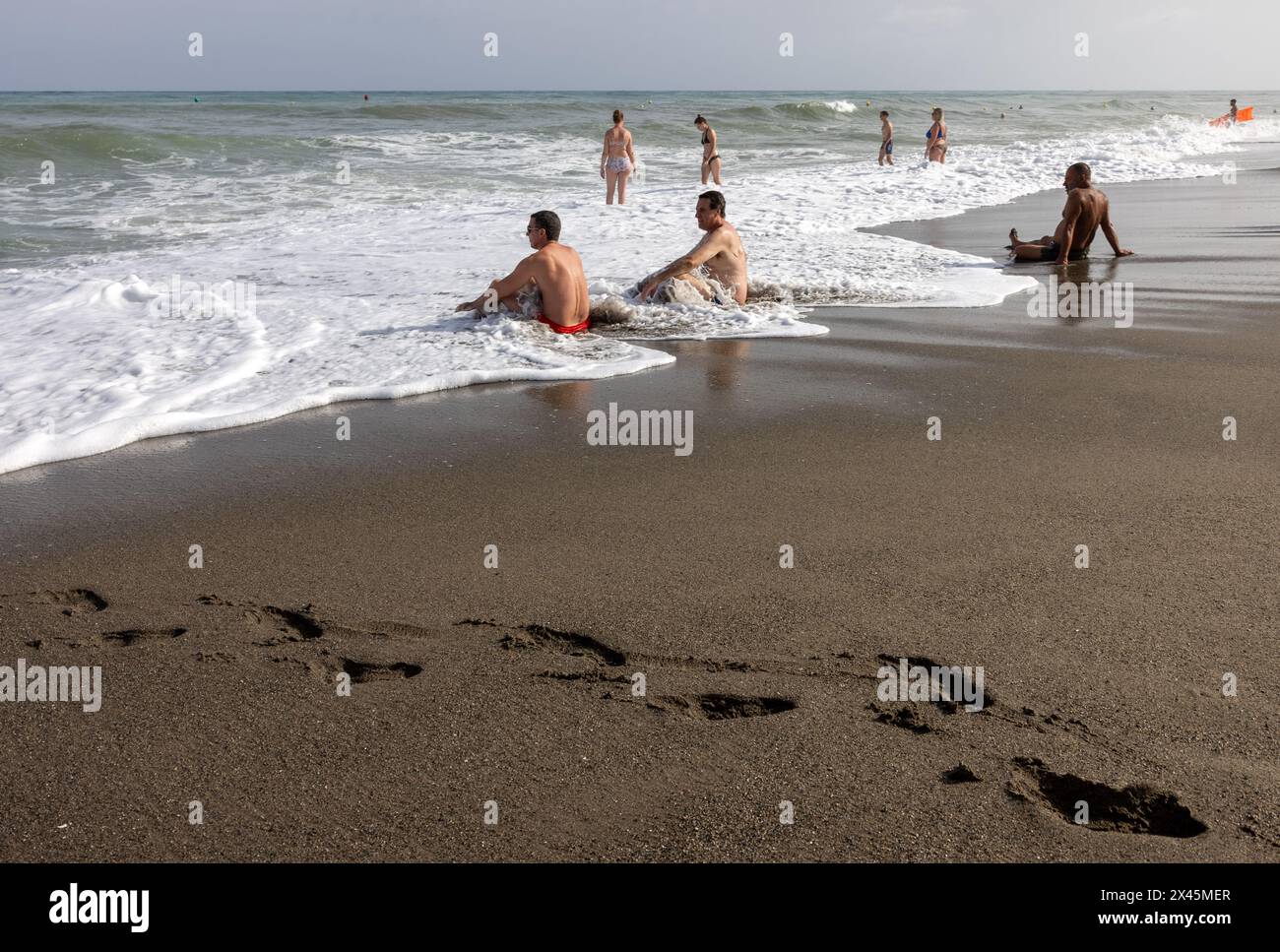 Torremolinos, Spain - September 14, 2023: Foamy sea waves and relaxing people on the sandy beach of Bajondillo in Torremolinos, Malaga, Costa del Sol, Stock Photo