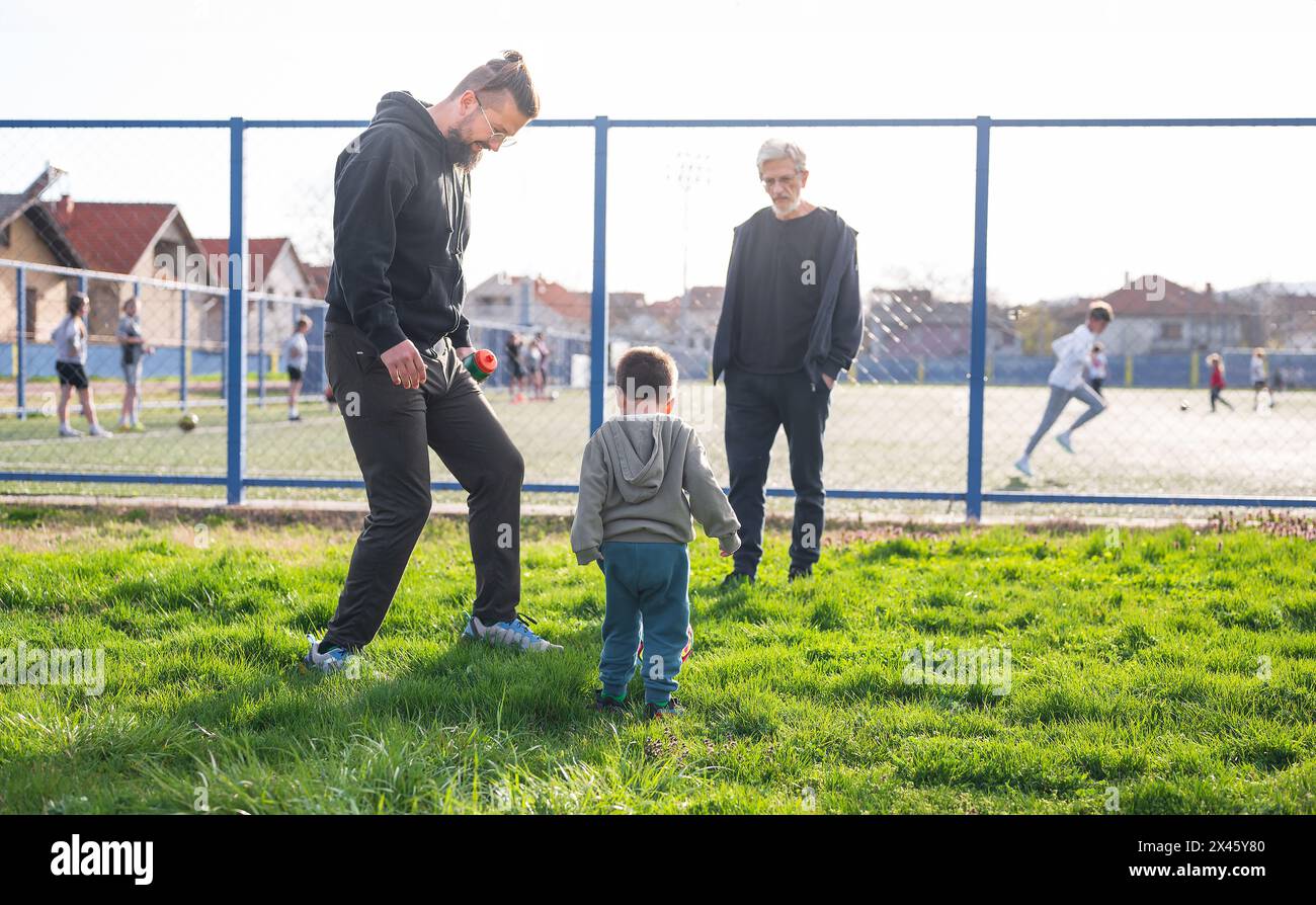 A toddler's football journey starts with family support on a grass field, engaging in an age-old sport at 3 years old Stock Photo