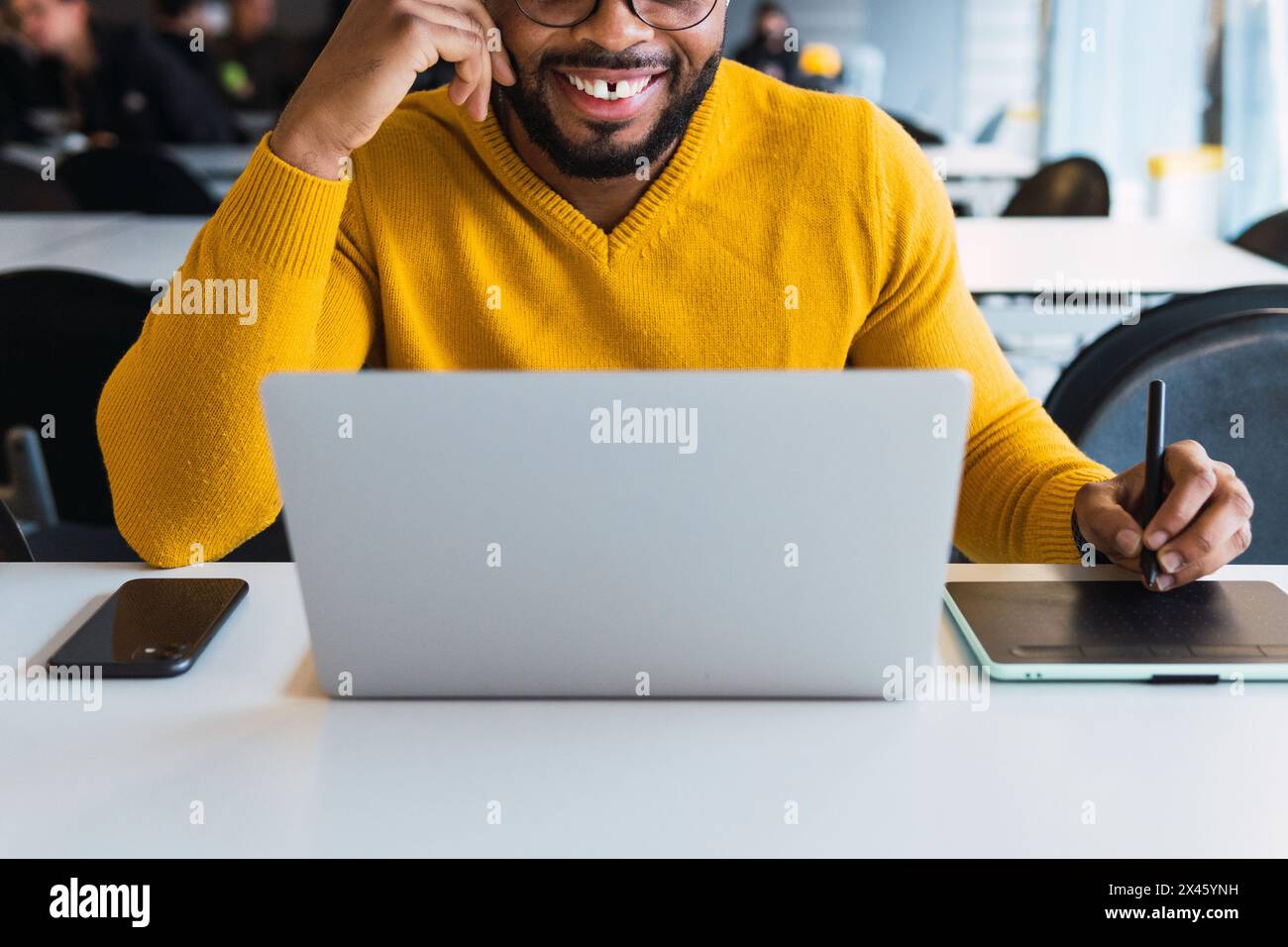 Cropped unrecognizable positive bearded African American male entrepreneur working on graphic tablet using stylus and on netbook in office Stock Photo