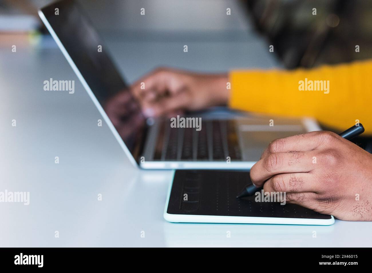 Cropped unrecognizable African American male entrepreneur working on graphic tablet using stylus and on netbook in office Stock Photo