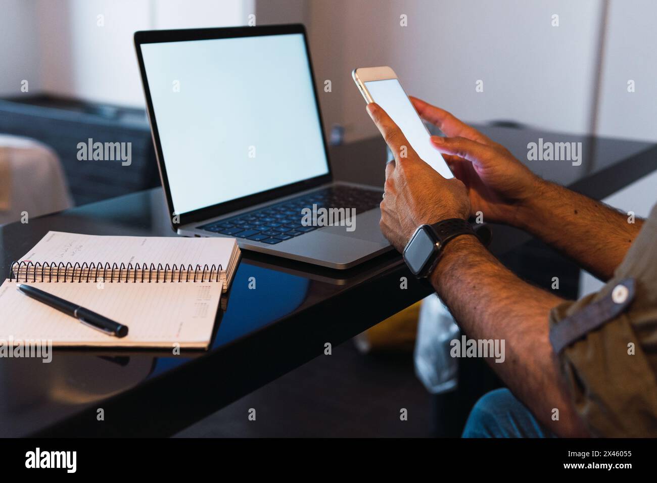 Crop unrecognizable male worker text messaging on cellphone with empty screen while sitting at table with netbook Stock Photo
