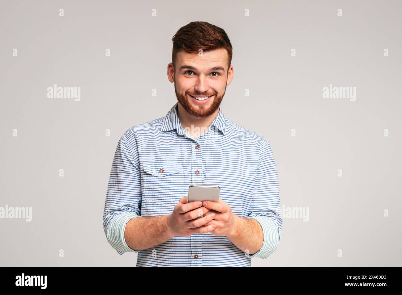Young bearded man using his phone and smiling Stock Photo
